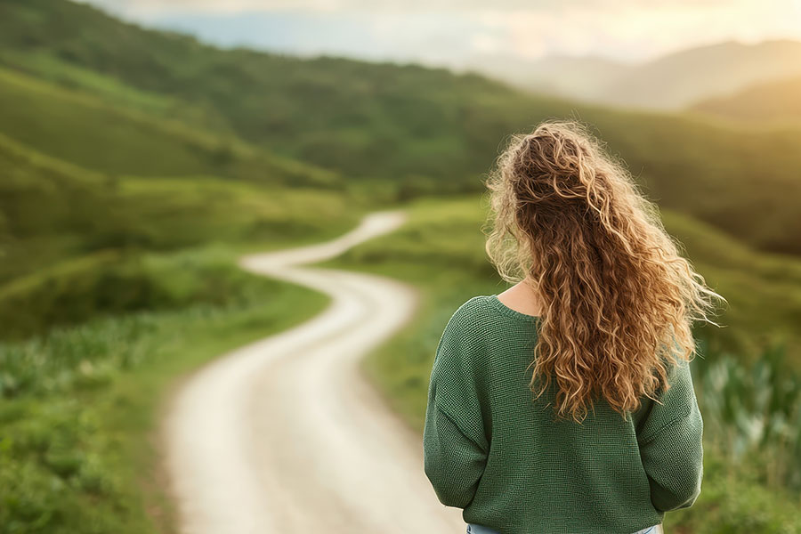 A young woman with curly hair walking down a serene winding road